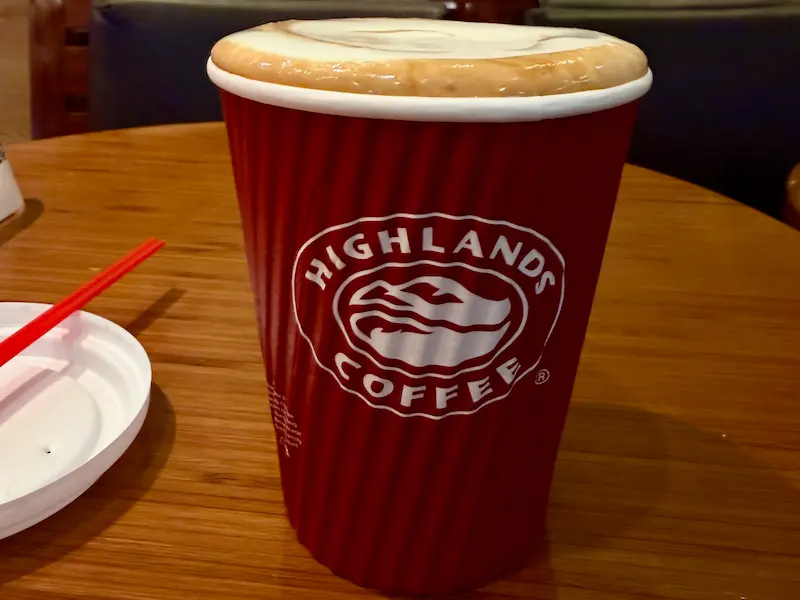 Красный бумажный стакан Highlands Coffee с густой взбитой пенкой на деревянном столе. Вьетнамский соленый кофе Ca Phe Muoi.