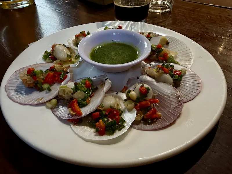 Тарелка с запеченными на гриле морскими гребешками в раковинах под соусом из зеленого лука и чили. В центре — пиала с традиционным вьетнамским зеленым соусом для морепродуктов. Свежие морепродукты в ресторане Нячанга.