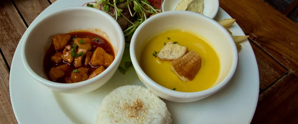 Крупный план аппетитного комбо-обеда с желтым крем-супом, мясным рагу и рисом на белой тарелке в ресторане Нячанга.