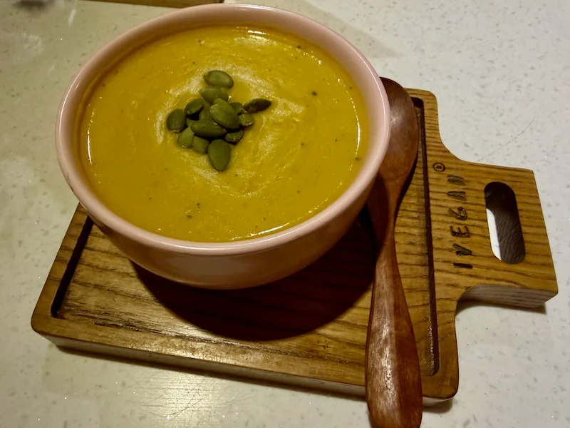 Густой веганский тыквенный крем-суп на кокосовом молоке с зелеными семечками в розовой миске на деревянной доске IVEGAN в Нячанге
