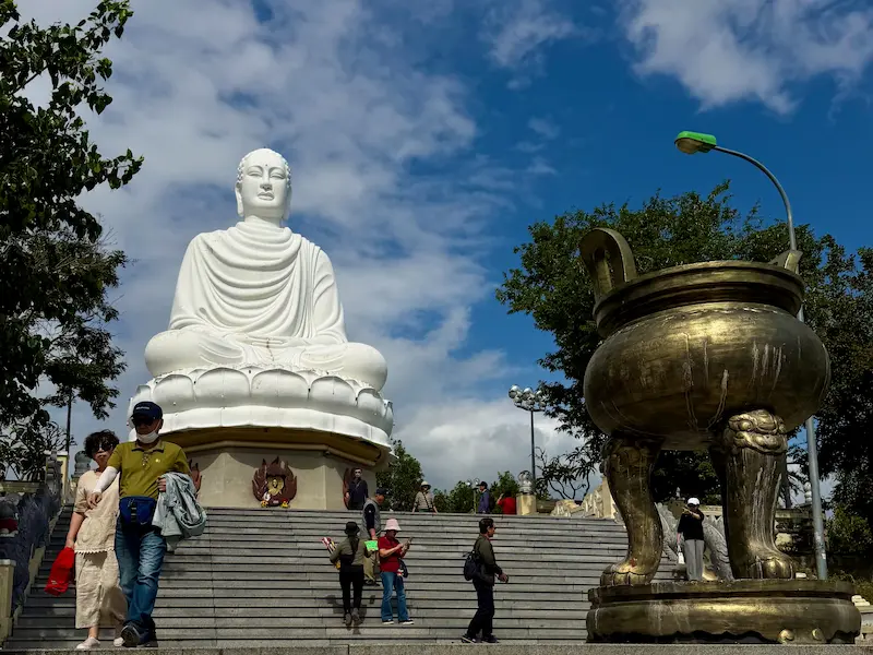 Величественная белая статуя сидящего Будды на вершине холма в пагоде Лонг Шон, Нячанг, с видом на лестницу и бронзовую курильницу для благовоний.