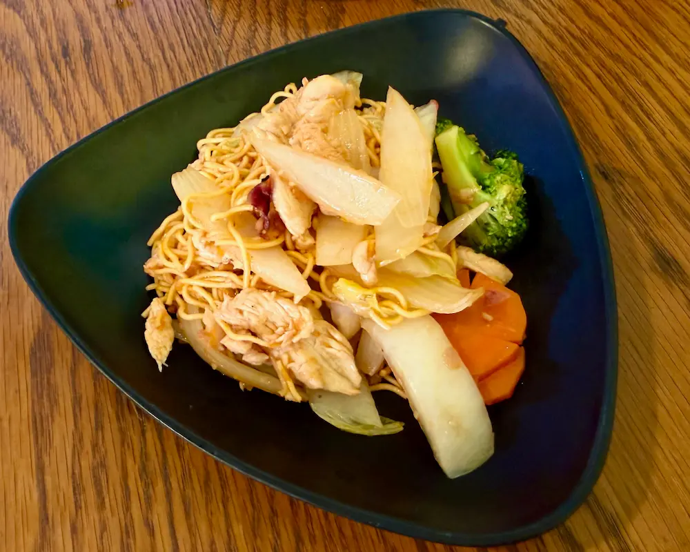 Традиционная вьетнамская жареная лапша с курицей и овощами (Mì xào gà) в темной тарелке на столе в кафе в Нячанге, Вьетнам